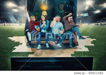 Soccer football fans sitting on the sofa and watching TV in the middle of a football field. 40911382