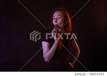 young woman smoking electronic cigarette on dark background 40914301