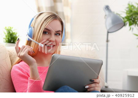 young beautiful blond woman sit on the sofa in livingroom hold tablet in arms listen to music sunny 40925912