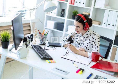 Beautiful young girl is sitting in headphones and with a microphone at the desk in the office. Beautiful young girl is sitting in headphones and with a microphone at the desk in the office. 40948002