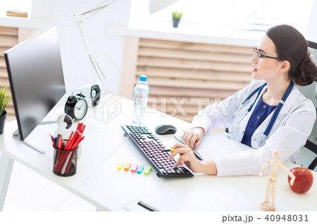 A beautiful young girl in a white robe is sitting at a computer desk with documents and a pen in her 40948031