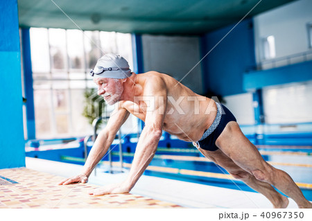 Senior man stretching by the indoor swimming pool. 40967350
