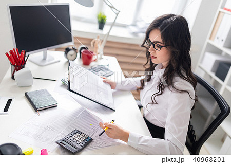 A young girl sits at the office desk and checks documents. 40968201