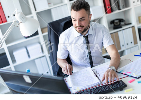 A man is sitting at a table in the office, working with documents and a computer. 40969124