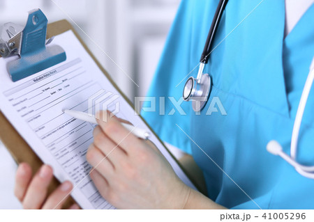 Female doctor filling up medical form on clipboard closeup. Physician finish up examining hi Female doctor filling up medical form on clipboard closeup. Physician finish up examining hi 41005296