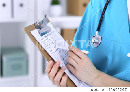 Female doctor filling up medical form on clipboard closeup. Physician finish up examining hi Female doctor filling up medical form on clipboard closeup. Physician finish up examining hi 41005297