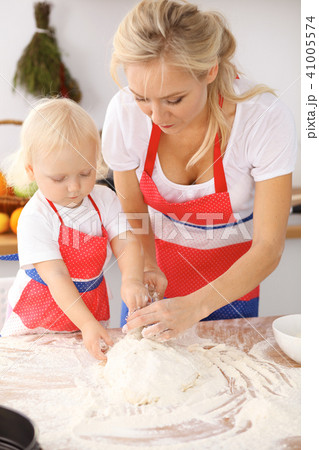 Little girl and her blonde mom in red aprons playing and laughing while kneading the dough in th Little girl and her blonde mom in red aprons playing and laughing while kneading the dough in th 41005574
