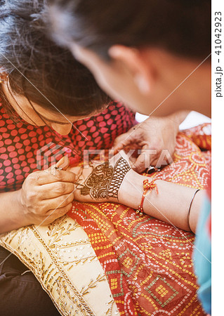 Henna artist (Mehndi) painting the hand of women Henna artist (Mehndi) painting the hand of women 41042923