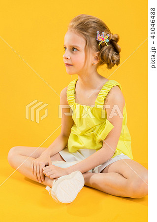 A teenage girl is sitting on a yellow background. 41046488