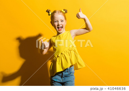 Girl with red hair on a yellow background. The girl laughs and shows the class sign. 41046636