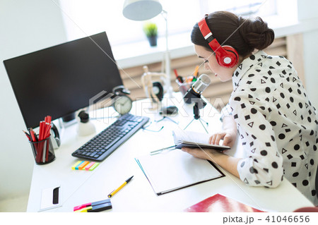 Beautiful young girl sits in headphones and with a notepad at the table in the office and speaks 41046656