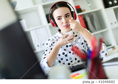 Beautiful young girl sitting in headphones at desk in office, eating yogurt and looking at monitor. 41046682