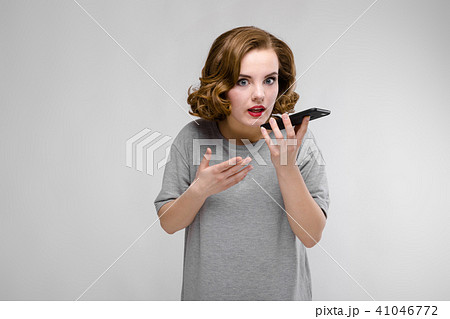 Charming young girl in a gray T-shirt on a gray background. The girl speaks by phone 41046772