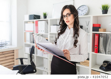 Beautiful young girl stands in the office thumbs a folder with documents. 41047052