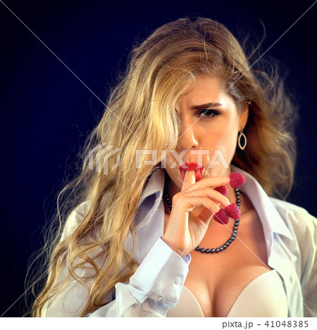 Woman eating berry. Pin up girl wearing unbuttoned blouse and bra. 41048385