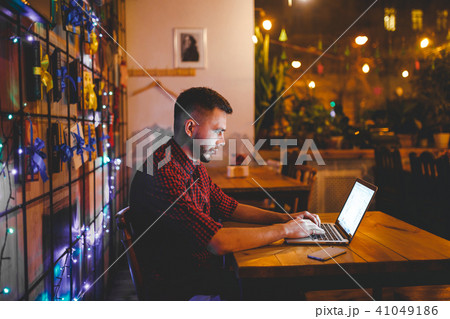 A young handsome Caucasian man with beard and toothy smile in a red checkered shirt is working A young handsome Caucasian man with beard and toothy smile in a red checkered shirt is working 41049186
