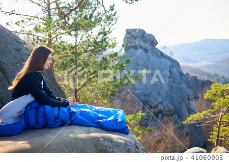 Woman sitting alone in sleeping bag on big mountain rock and smiling 41060903