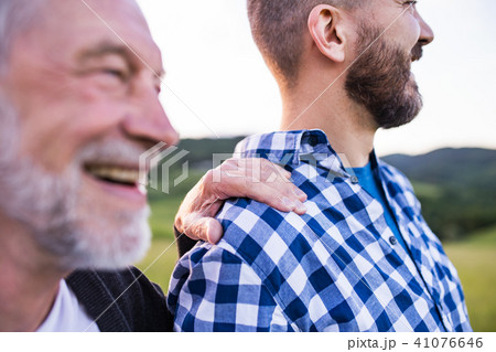 An adult hipster son with senior father on a walk in nature at sunset. 41076646