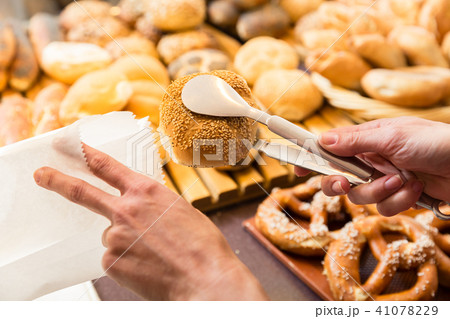 Sales woman in baker shop putting bread roll in paper bag Sales woman in baker shop putting bread roll in paper bag 41078229
