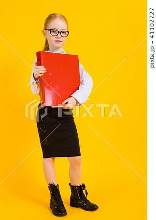 Girl with red hair on a yellow background. A charming girl in transparent glasses is holding a large Girl with red hair on a yellow background. A charming girl in transparent glasses is holding a large 41102727