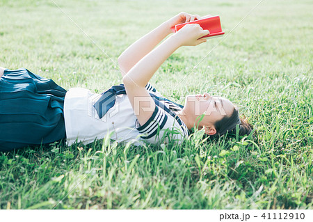 芝生に寝転がって本を読む高校生の写真素材