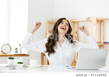 Successful business woman with arms up sitting in modern office. 41118048