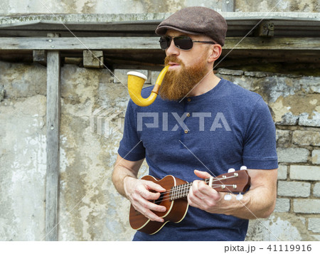 Man with beard playing ukulele and smoking a pipe 41119916