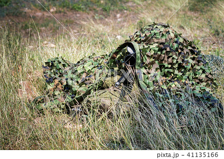 Sniper laying on the grass looking through scope. 41135166