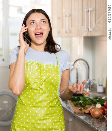 Girl housewife in apron talking by phone at home kitchen 41137989