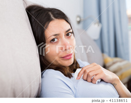 Sad young woman thinking on sofa in home interior Sad young woman thinking on sofa in home interior 41138651