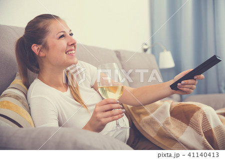 Young female is watching TV and sitting with white wine Young female is watching TV and sitting with white wine 41140413