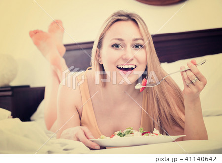 Blond woman in underwear sitting in the bed and enjoying a salad Blond woman in underwear sitting in the bed and enjoying a salad 41140642