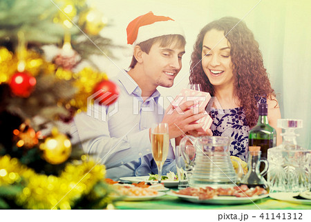 Man giving present to woman during Christmas dinner Man giving present to woman during Christmas dinner 41141312