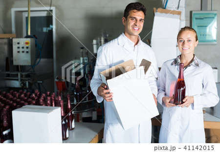 Two smiling employees standing in packaging section on wine manufactory 41142015