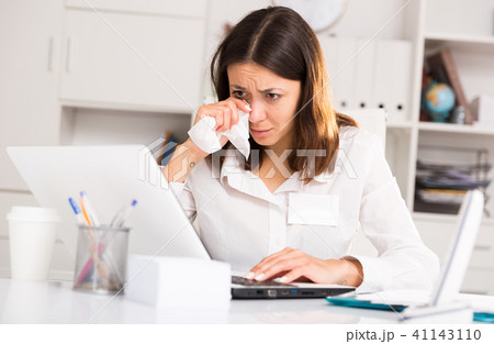 Unhappy girl holding napkin during work with laptop and documents Unhappy girl holding napkin during work with laptop and documents 41143110