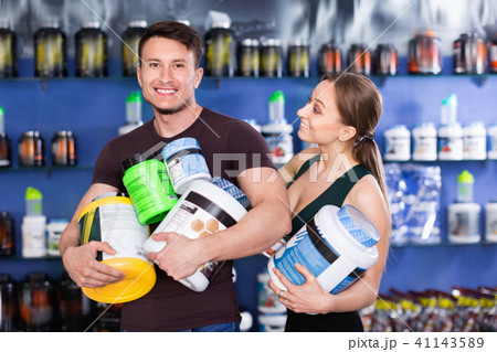 Happy young sporty people standing in store, holding big can of sport nutrition 41143589