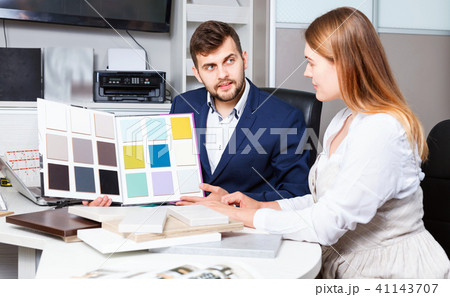 Competent seller in showroom helping young female client to choose furniture materials for her apartment Competent seller in showroom helping young female client to choose furniture materials for her apartment 41143707