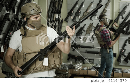 Young guys in military equipment with rifle in airsoft shop Young guys in military equipment with rifle in airsoft shop 41144579