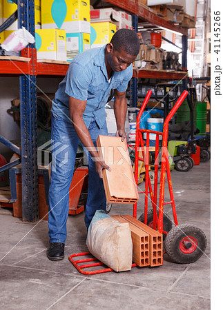 Serious African American putting construction supplies on handcart in building hypermarket 41145266