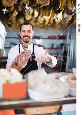 Male shop assistant demonstrating piece of meat in butcher’s shop Male shop assistant demonstrating piece of meat in butcher’s shop 41147519