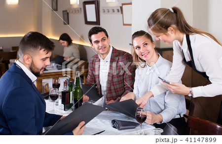 polite waitress bringing delicious salads to smiling people at restaurant 41147899