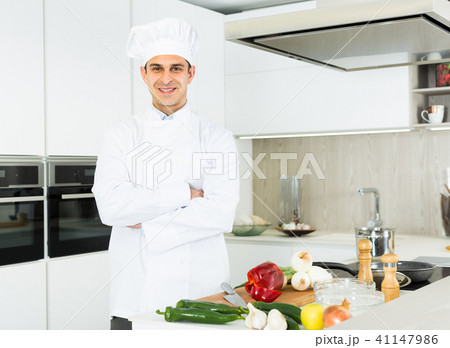 Smiling male kitchener in uniform is standing in the kitchen Smiling male kitchener in uniform is standing in the kitchen 41147986