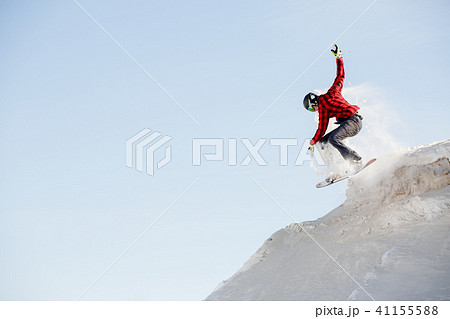 Photo of man in helmet with snowboard jumping from snowy mountain slope 41155588