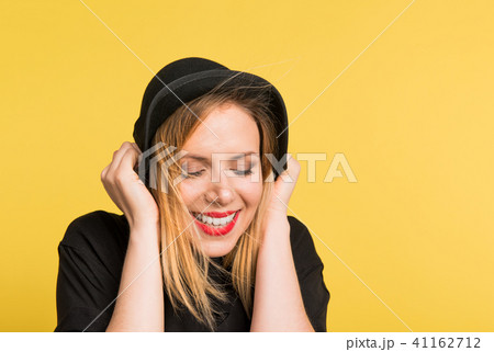 Portrait of a young beautiful woman with black hat in studio on a yellow background. 41162712