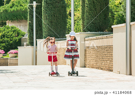 Preschooler girls riding scooter outdoors. 41184068
