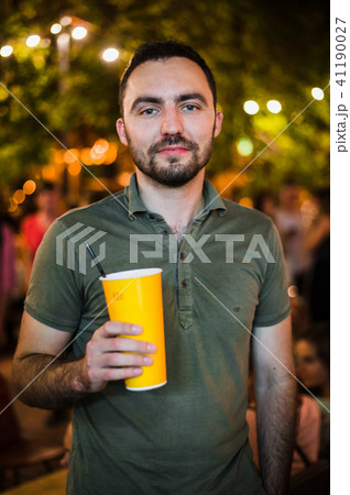 Handsome Bearded European Man Drinking coctail or beer at outdoor Street Cafe night party in park 41190027