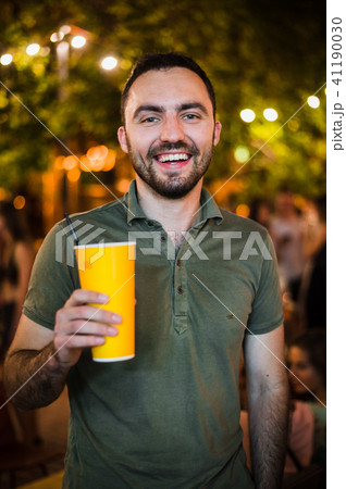 Handsome Bearded European Man Drinking coctail or beer at outdoor Street Cafe night party in park Handsome Bearded European Man Drinking coctail or beer at outdoor Street Cafe night party in park 41190030