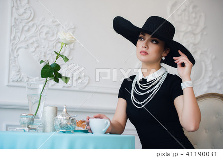 Woman in hat, much like the famous actress, croissant eating and drinking tea. Woman in hat, much like the famous actress, croissant eating and drinking tea. 41190031