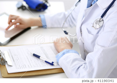 Woman doctor using tablet computer while sitting at the desk in hospital closeup. Cardiologist Woman doctor using tablet computer while sitting at the desk in hospital closeup. Cardiologist 41190341
