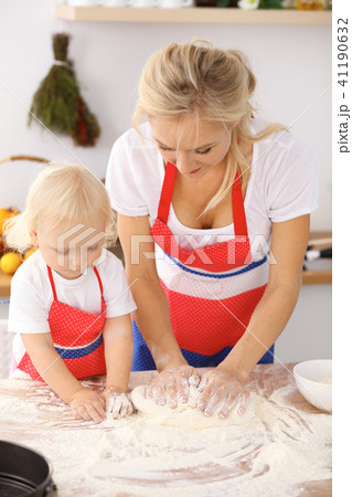 Little girl and her blonde mom in red aprons playing and laughing while kneading the dough in th Little girl and her blonde mom in red aprons playing and laughing while kneading the dough in th 41190632